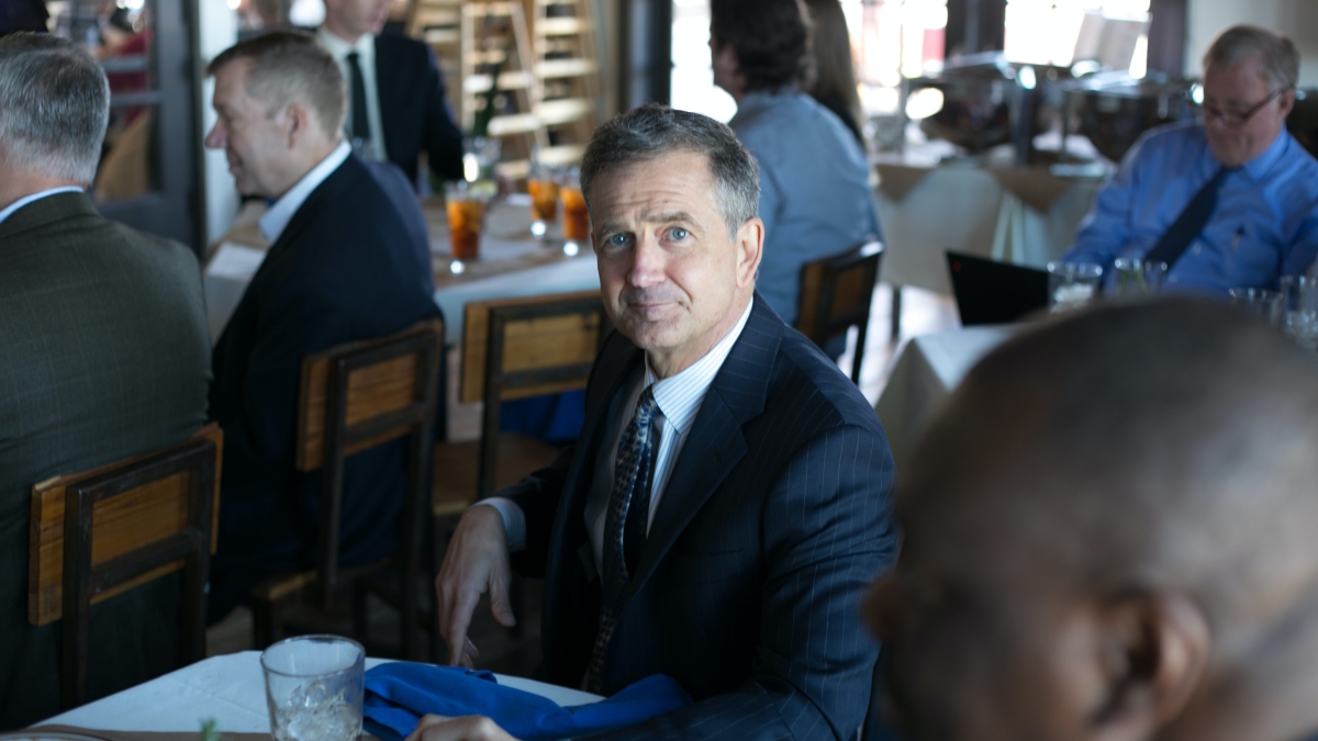 Stock photo of older man in dark suit sitting at table.