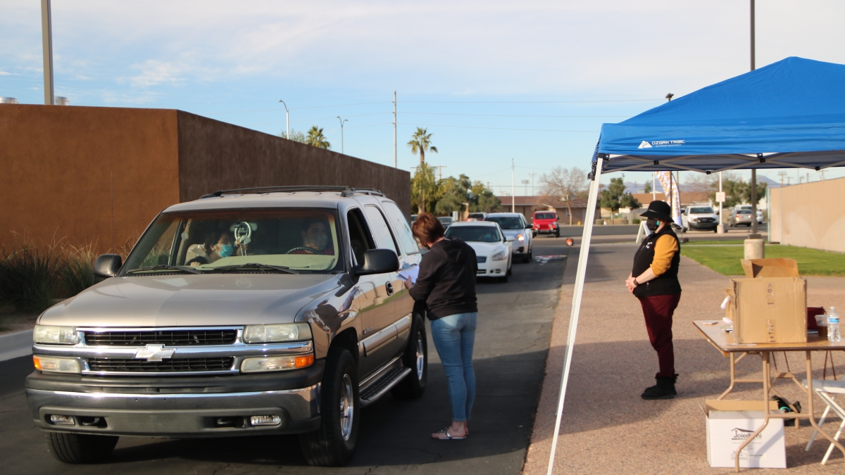 Two masked ASU employees help a line of cars at the Mesa Convention Center check in for FAFSA help