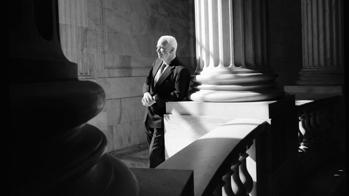 A black and white photo of Sen. John McCain leaning on a column and looking to the side