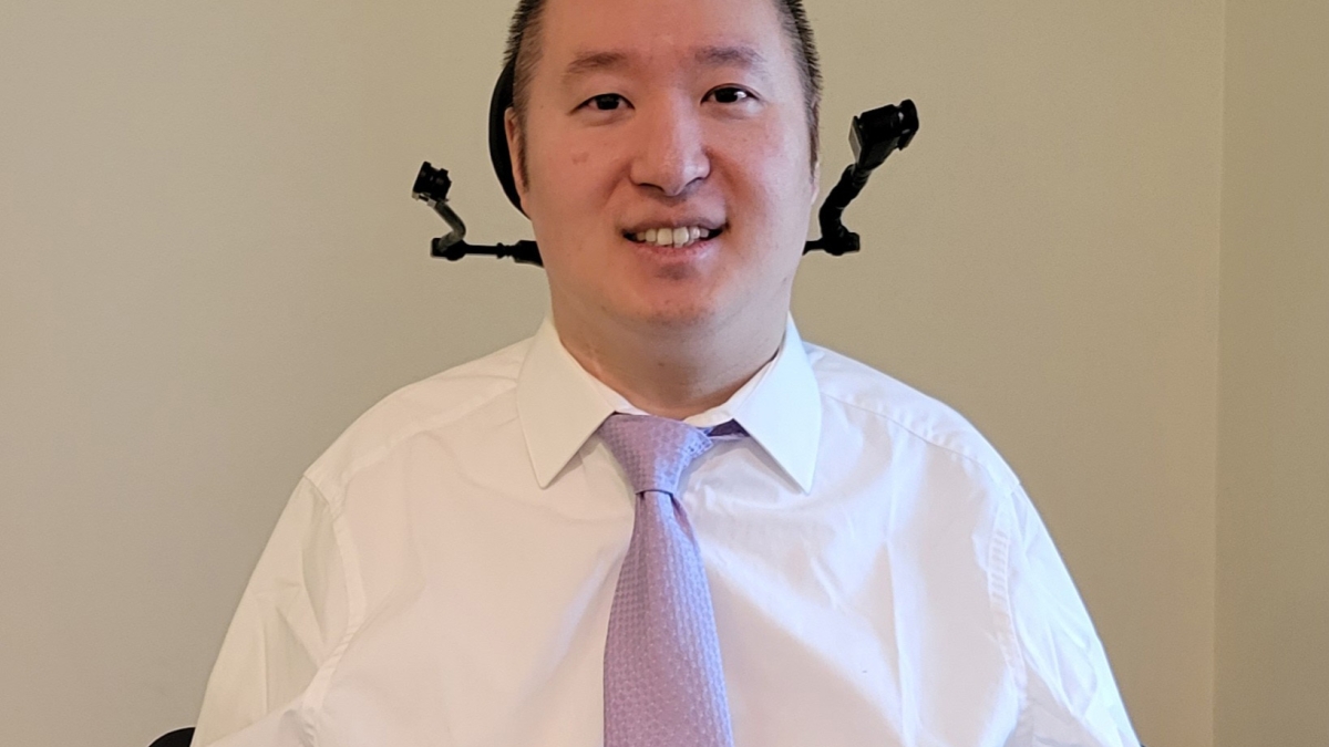 Portrait of Jonathan Ko sitting in a chair and wearing a tie, smiling.