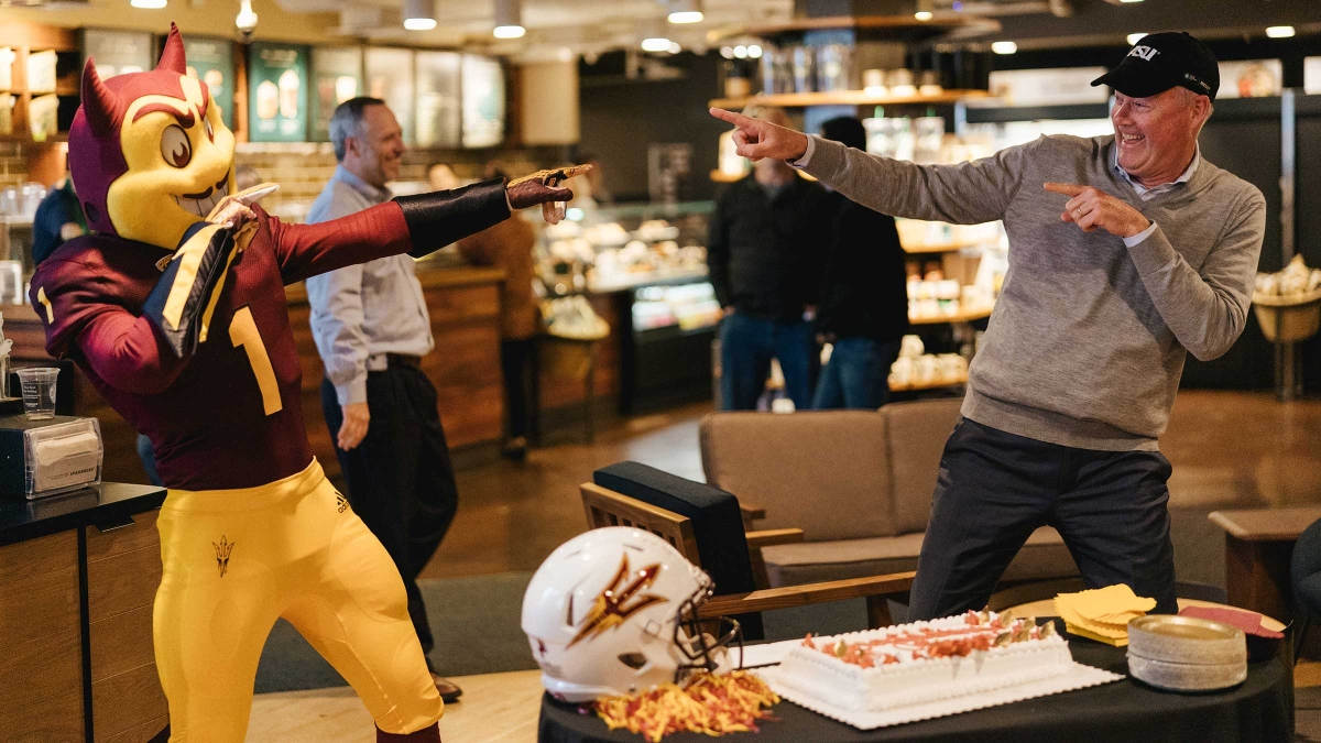 Sparky and Starbucks CEO Kevin Johnson point at each other at a fifth-anniversary celebration