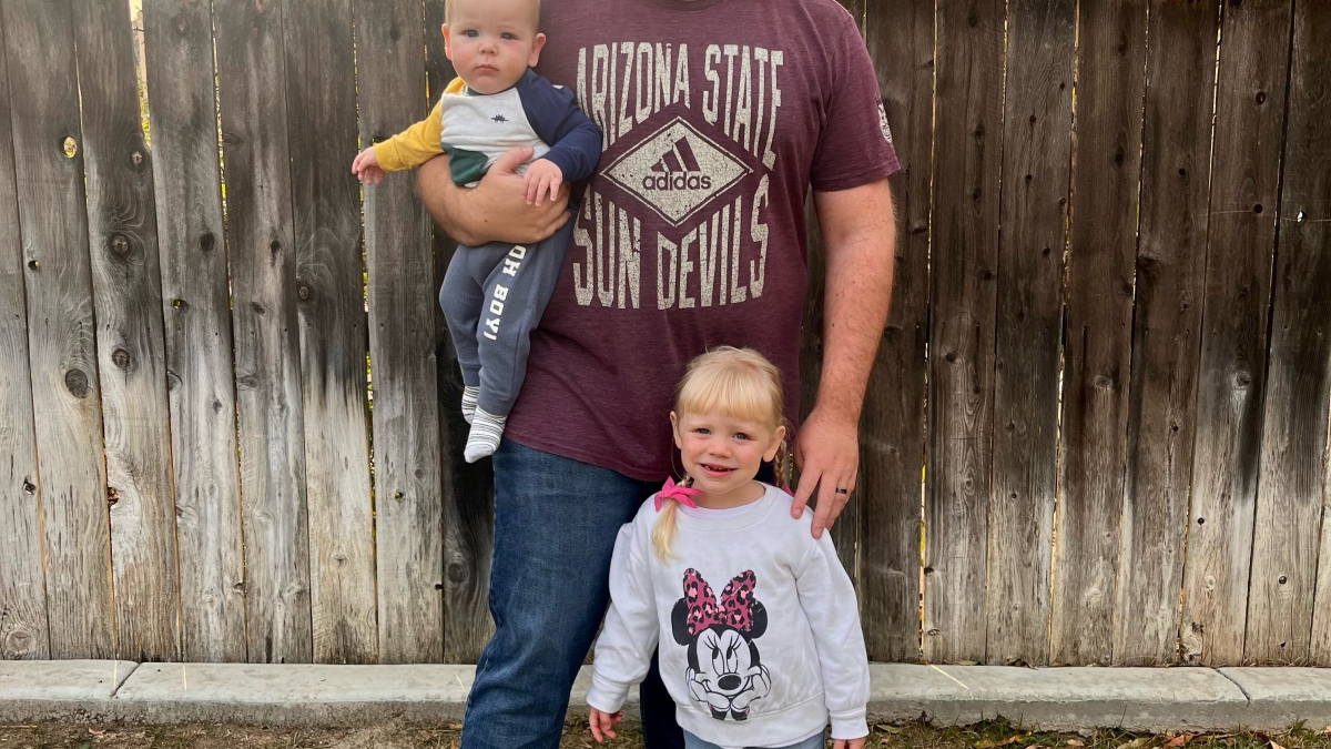 Kyle Durrschmidt, ASU Online graduate, stands with two children in front of an outdoor wooden fence
