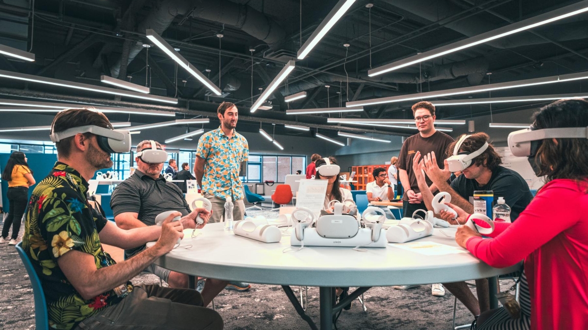 A group of people sit at a table together, interacting with virtual reality headsets.