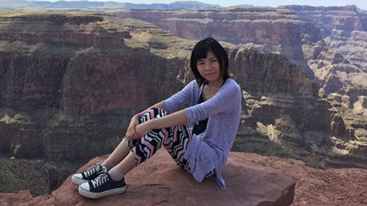 Lihong Ou sits on a rock with the Grand Canyon behind her. She's wearing a purple sweater, black and white tights and black and white sneakers.