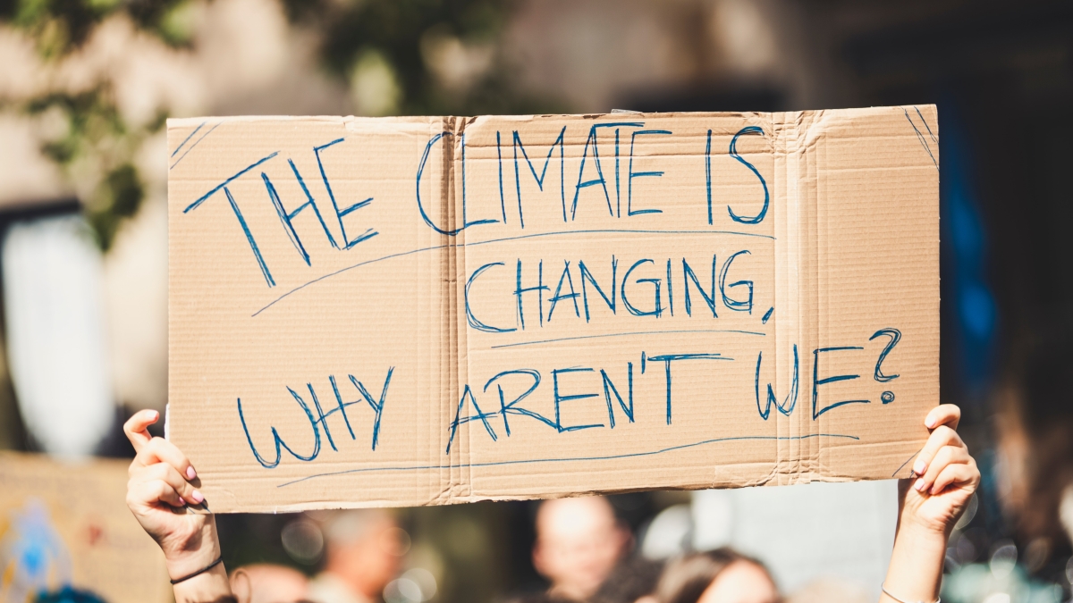 A cardboard sign that reads "THE CLIMATE IS CHANGING, WHY AREN'T WE?"
