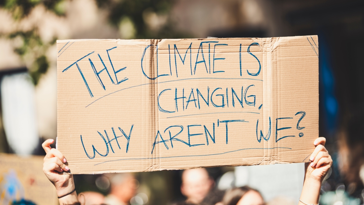 A cardboard sign that reads "THE CLIMATE IS CHANGING, WHY AREN'T WE?"