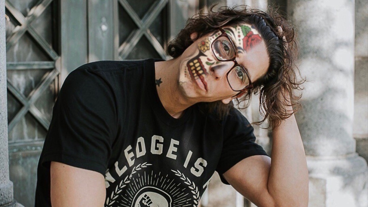 Mathew Sandoval wearing Day of the Dead face paint and sitting on a step.