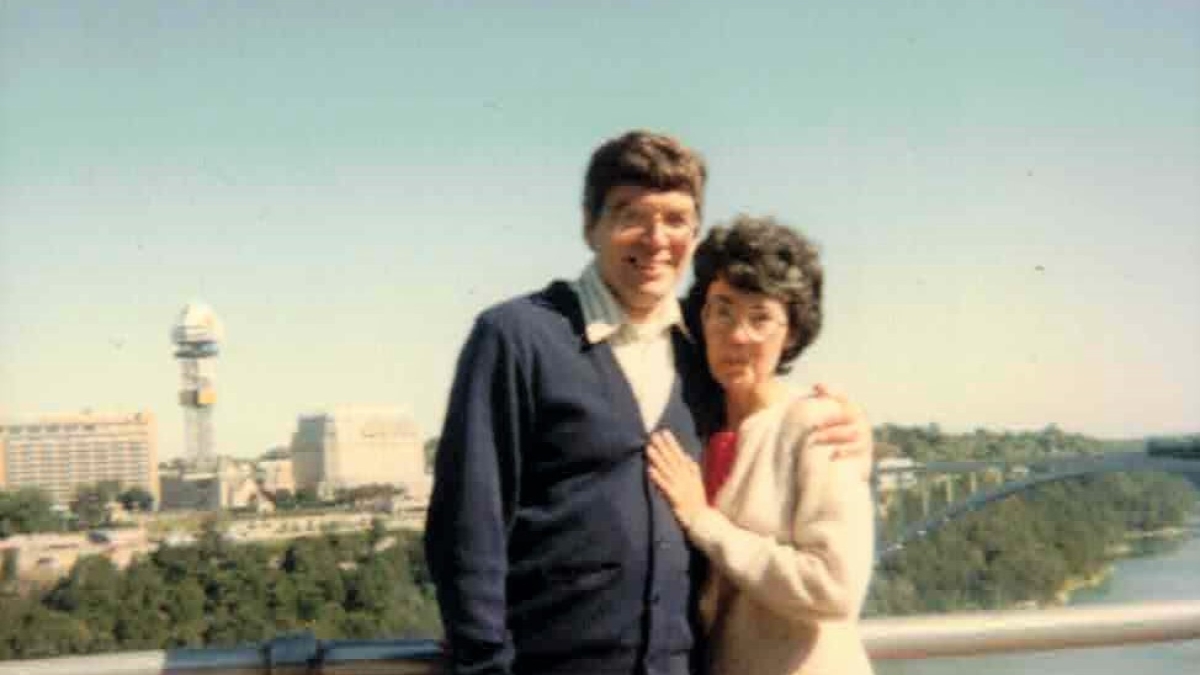 A man and a woman pose together on a bridge.