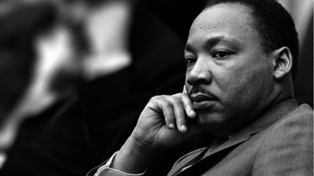 A black-and-white photo of Martin Luther King Jr. sitting and thinking.