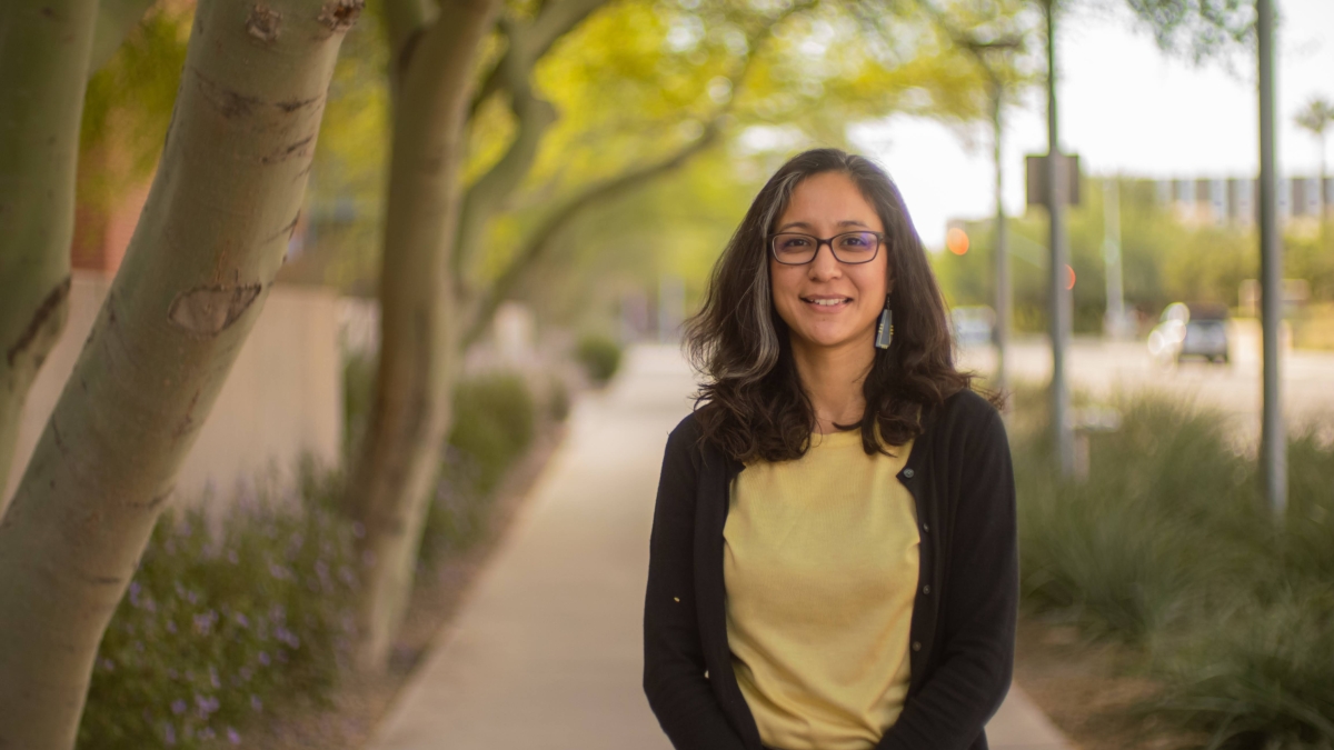 ASU Assistant Professor Viridiana Benitez smiling, looking at the camera, on a sidewalk lined with trees and bushes.