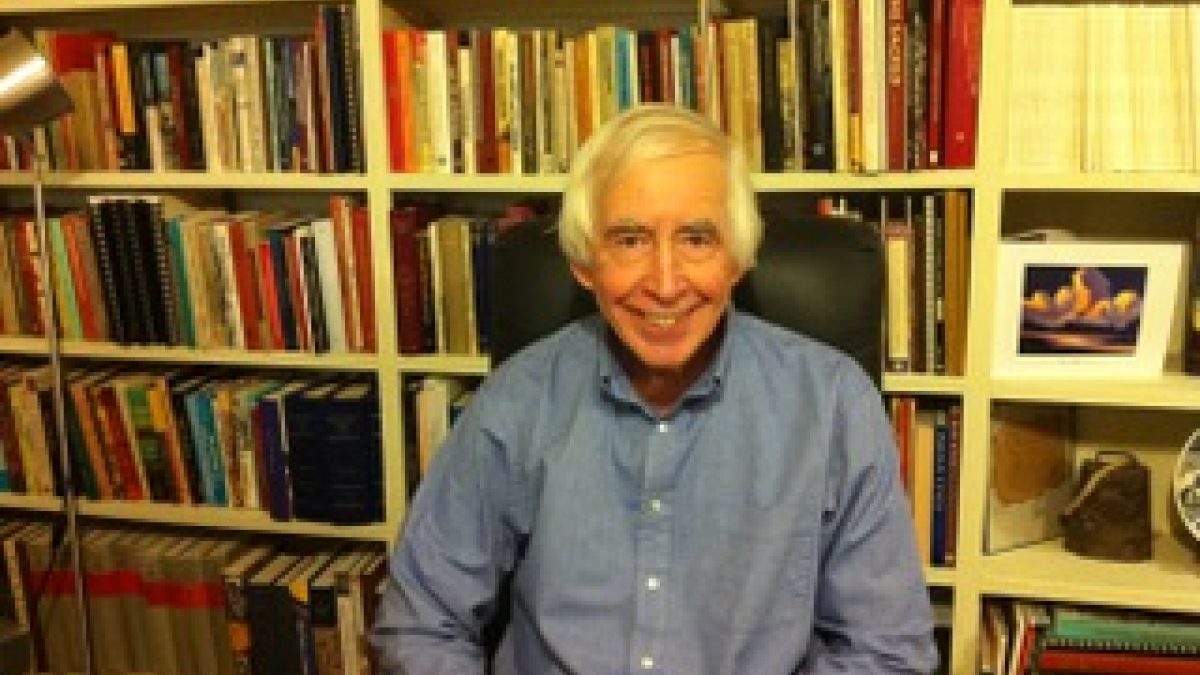 Professor Peter James Iverson smiles at the camera while sitting in front of a full bookcase