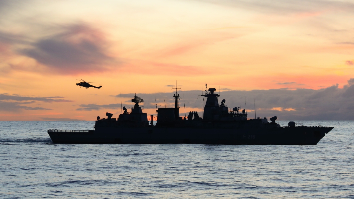 Navy ship sailing in front of a sunset on the water.