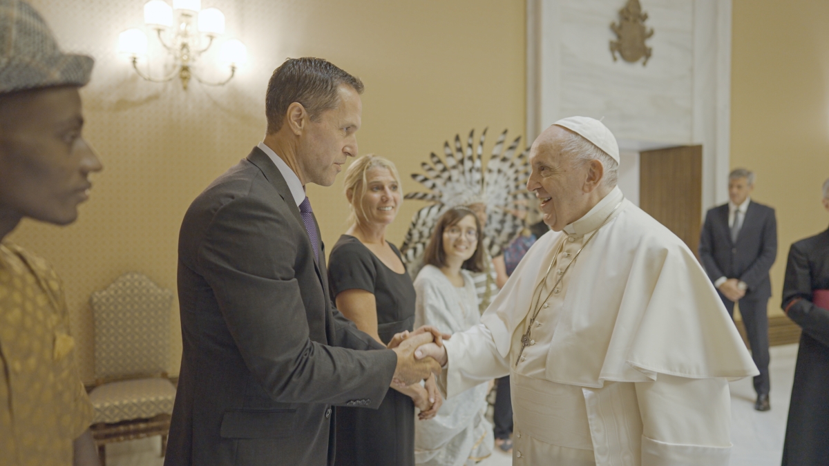 Man dressed in a suit shaking hands with Pope Francis.
