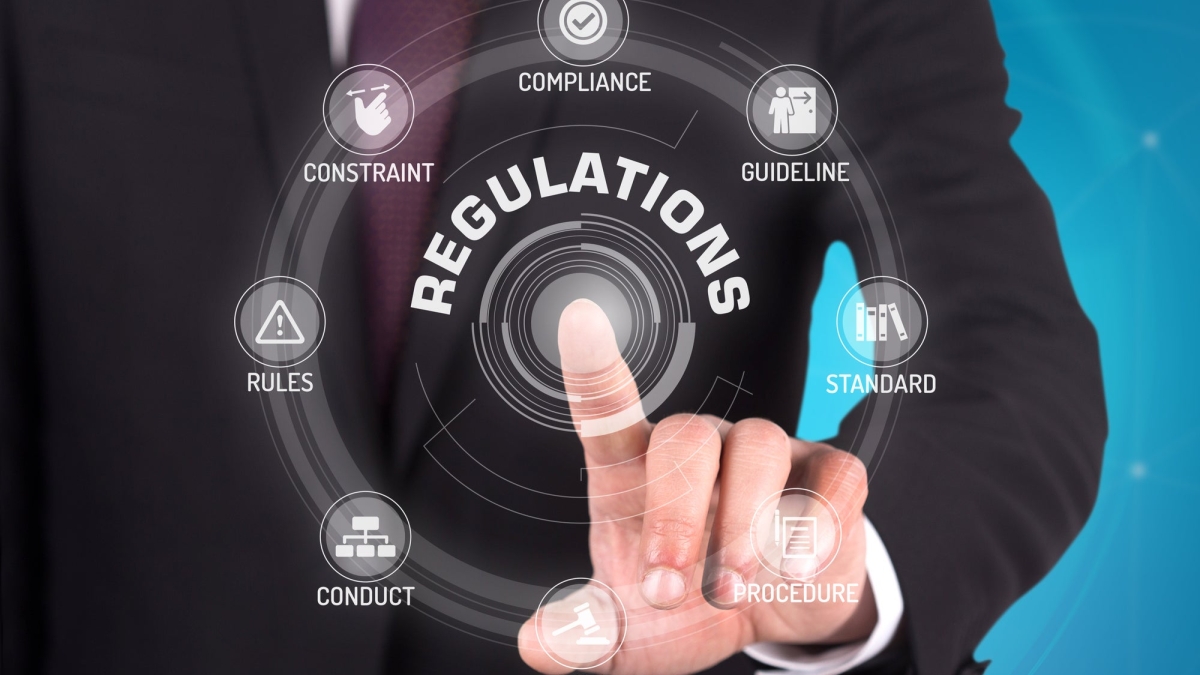 A man in suit with only his arm visible taps a screen with the word "regulations" on it.