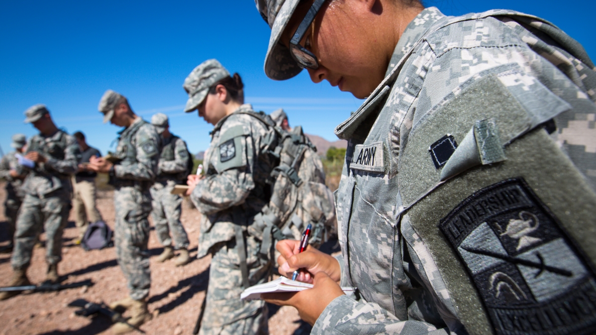 Army soldiers in fatigues take notes in a desert landscape