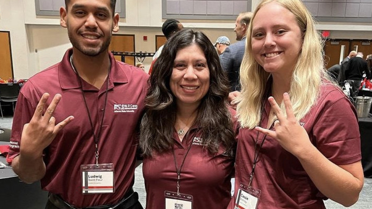 Two ASU business students and an ASU faculty member smile and make a pitchfork symbol with their hands.