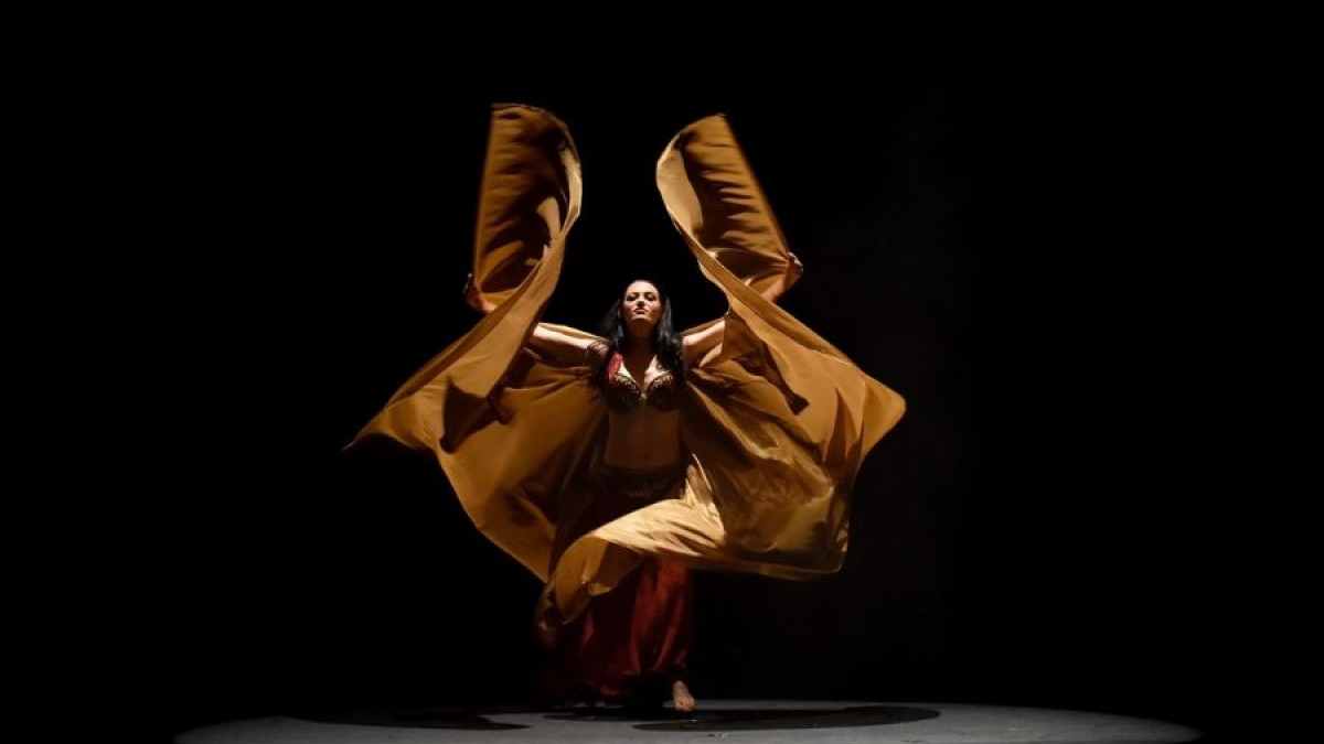 belly dancer is shown in an dramatic pose in a gold winged costume