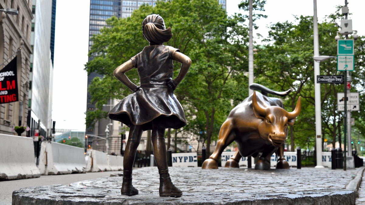 Statue of little girl standing with hands on hips in front of statue of large bull on Wall Street