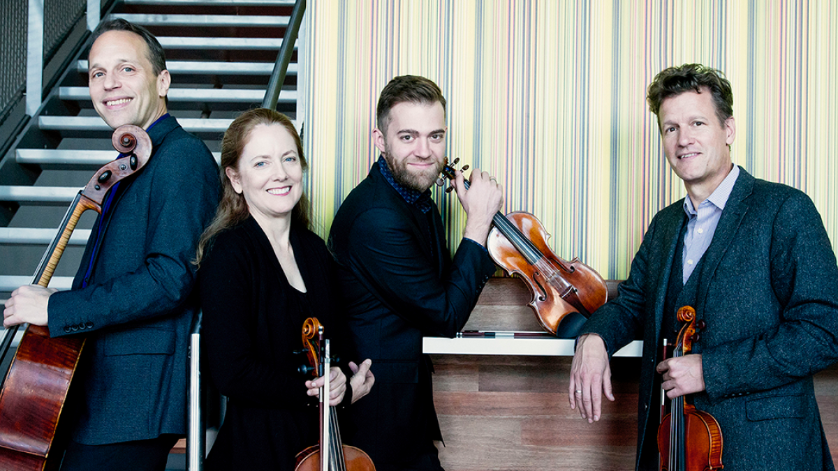 Four musicians pose for a photo holding their string instruments