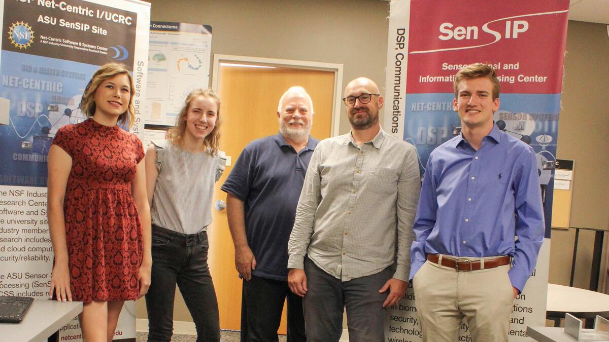 ASU Profesor Andreas Spanias poses for a group photo with teachers and students in front of banners with information about eduactional outreach programs.