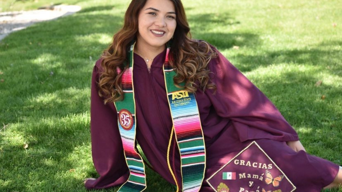 Picture of Maricela Diaz in cap and gown sitting on green grass in the shade