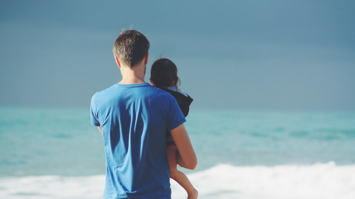 A father holds his child in front of the ocean.