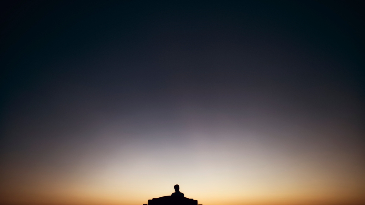 An image of a person sitting alone on a bench at sunset