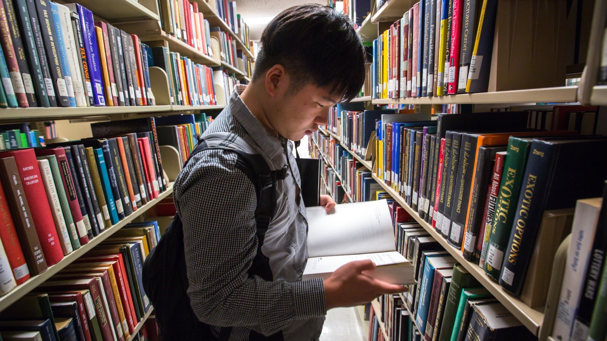 A student looks at book in Hayden Library bookshelves