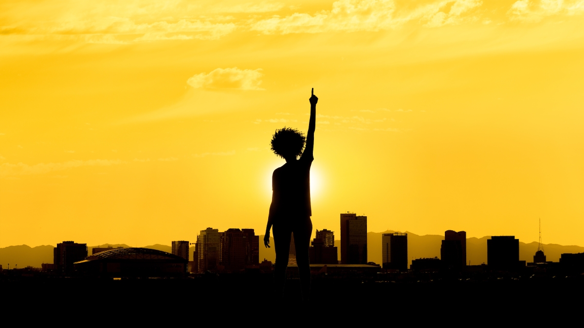 A woman holds up hand against a silhouetted sunset skyline