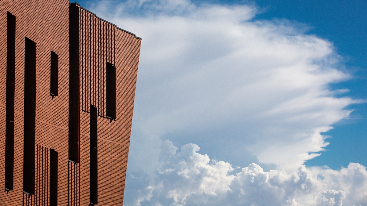 An edge of a brick building is shown against a blue sky with fluffy clouds