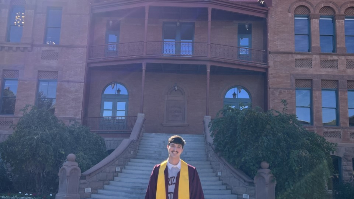 ASU grad Ryan Bieniek wearing gradution regalia at the bottom of the Old Main building staircase.