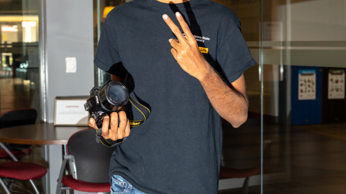 Venu Gopinath Nukavarapu in the MU with a mask, an ASU Student Life shirt and his camera giving a peace sign