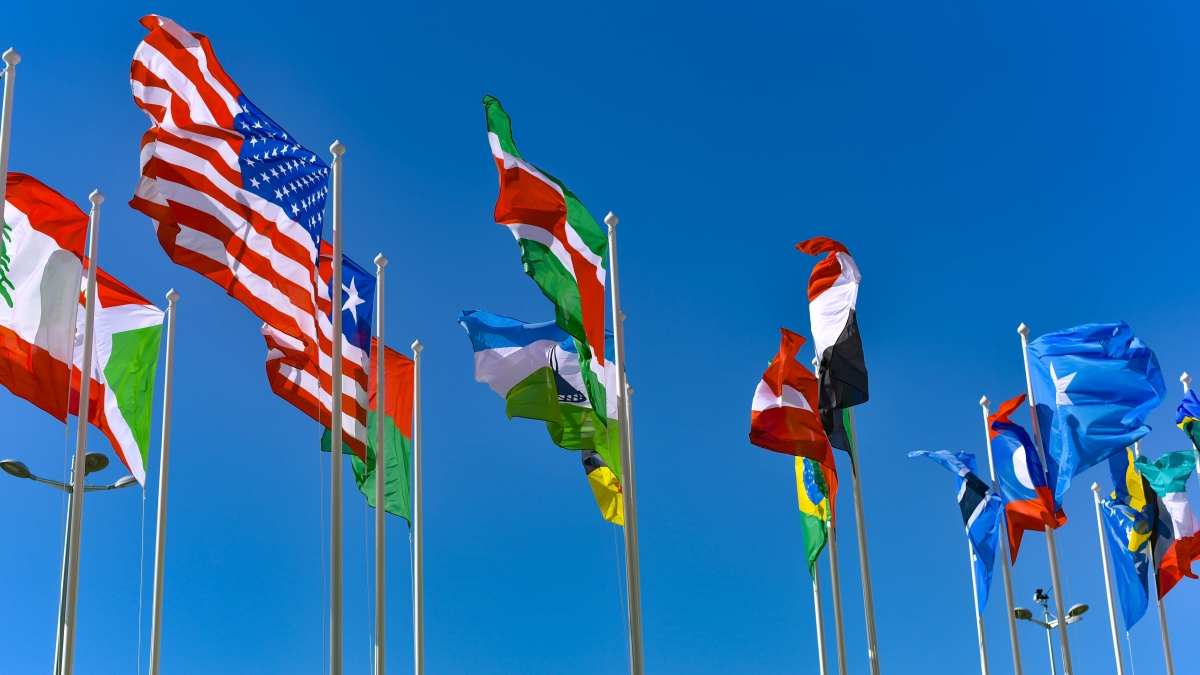 Flags of various countries flying in the wind against the backdrop of a bright blue sky.
