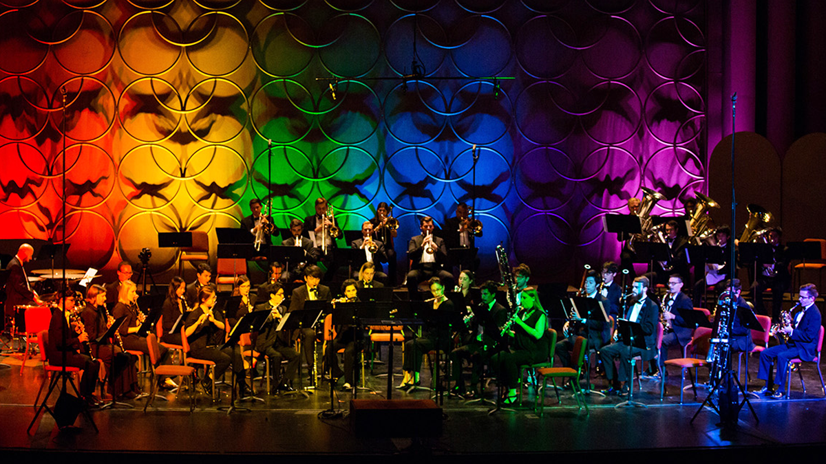 Wind band performing on a stage lit up with many colors.