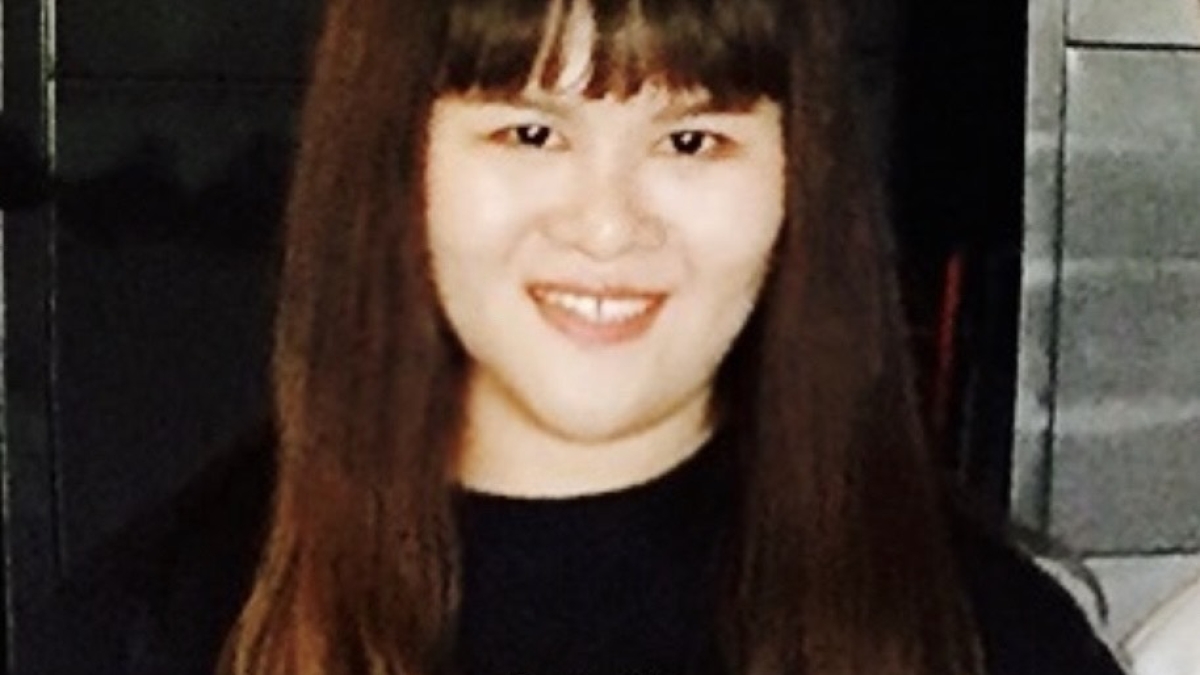 Yishu Li smiles at the camera. She has fair skin and medium-length dark hair with bangs that cover her forehead. She is wearing a black long-sleeve shirt with Keith Haring-inspired art on the front of a red heart and several stick figures.