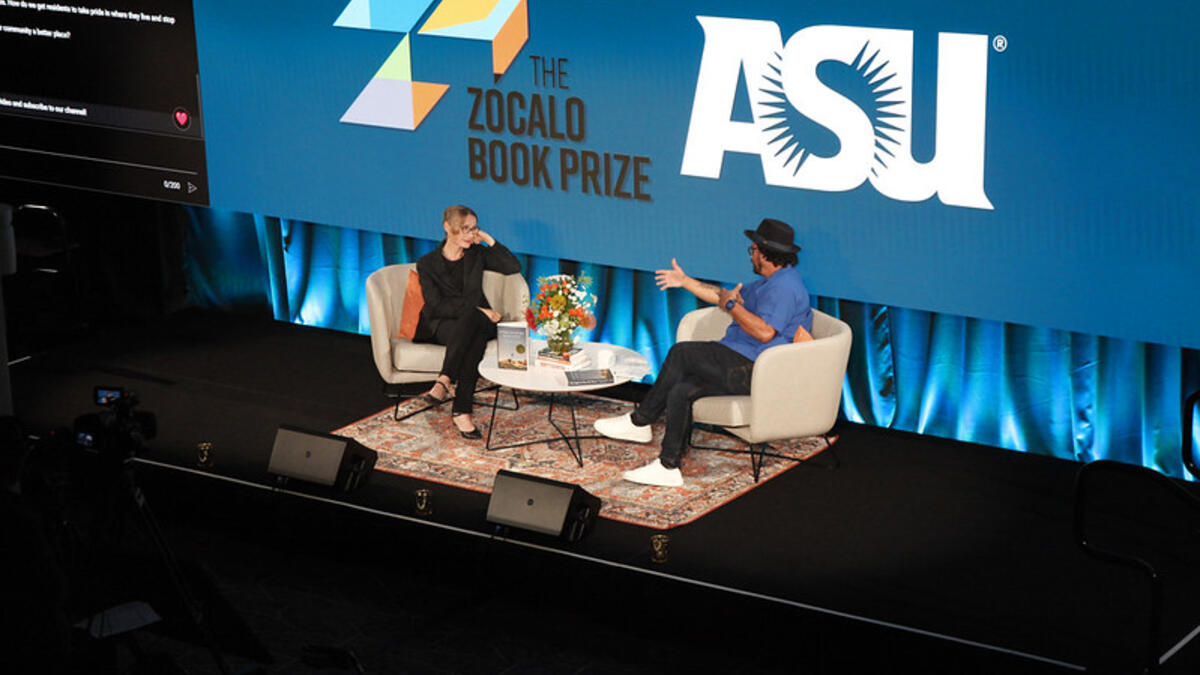Two people sit on stage across from each other with an ASU Zocalo Book Prize sign behind them.