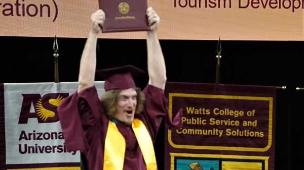 A graduate holds his diploma cover over his head at the spring 2023 Watts College convocation.