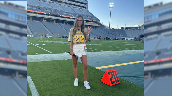 ASU grad Courtney Robinson makes the ASU pitchfork sign on a football field.