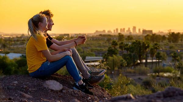 Two people sit on a rock and watch the sunset