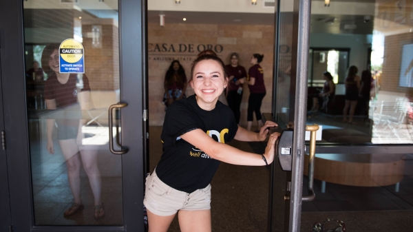 A female student opens a dorm lobby door in welcom at West campus move-in