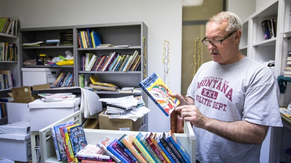 professor holds a book in office full of books 