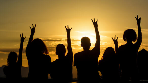 students with hands in air making pitchfork sign in front of sunset