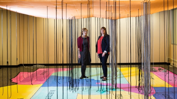 two women standing on exhibit of AZ map on floor with black strings hanging from ceiling