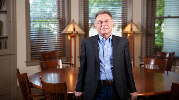 Portrait of ASU Regents Professor Alberto Rios. Rios is leaning against a round table in a room with three windows and two antique lamps.