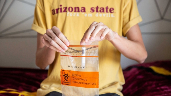 A student puts a saliva test tube into a sealable bag for COVID19 testing