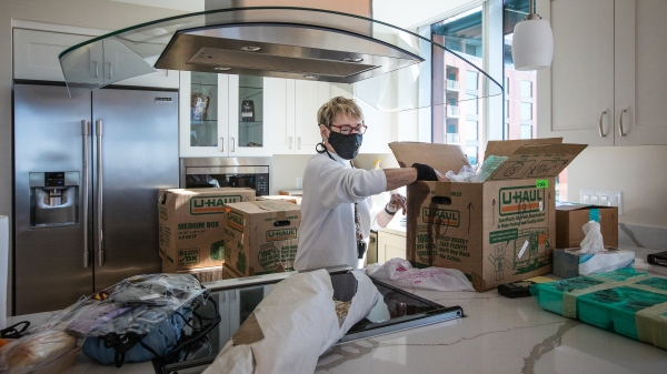 A woman in a mask unpacks boxes in her new kitchen