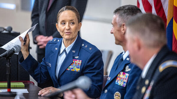 A female military officer holds up a piece of paper as she speaks to two male military officers during a panel