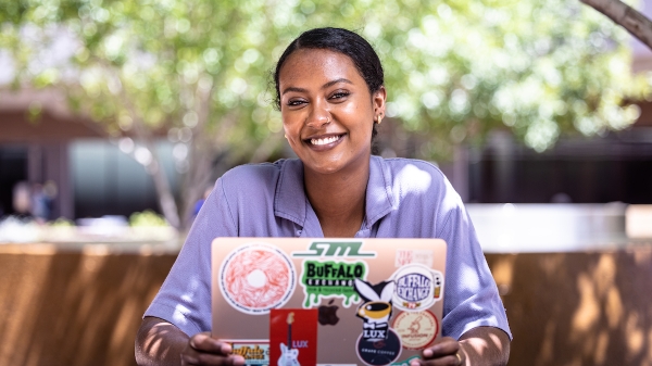 Sabrina Mehari, a student at ASU's Barrett, The Honors College, smiling while seated at a picnic table with a laptop.