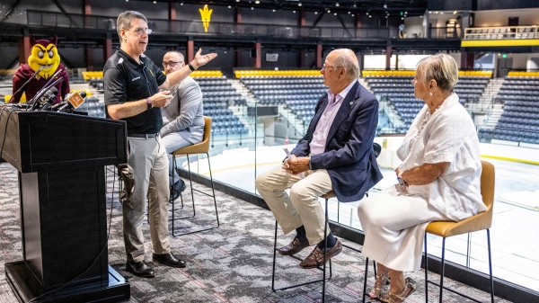 Man talking to two people sitting in chairs inside hockey arena for event