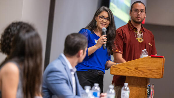 Two moderators standing behind a lectern talking to event panelists.